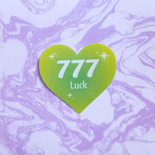 Load image into Gallery viewer, Green gradient heart-shaped sticker with '777 Luck' white text on a purple and white marbled background.
